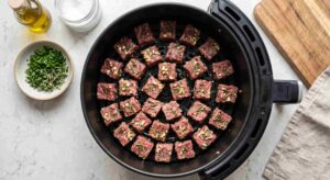 Raw seasoned steak cubes placed inside a black air fryer basket